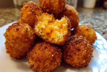 A close-up of golden-brown, crispy Cheesy Mashed Potato Balls, one of which is broken open revealing melted cheddar cheese inside.