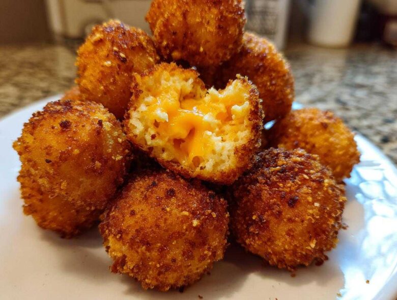 A close-up of golden-brown, crispy Cheesy Mashed Potato Balls, one of which is broken open revealing melted cheddar cheese inside.