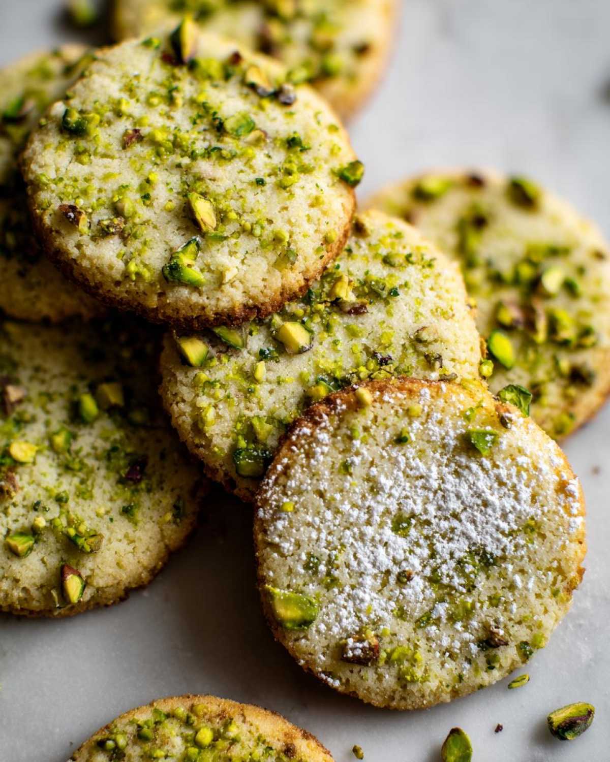 A close-up stack of chewy Pistachio Cookies topped with bright green chopped nuts and powdered sugar.