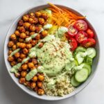 Overhead view of a colorful Chickpea Grain Bowl with avocado lemon tahini dressing drizzled over seasoned chickpeas and quinoa.