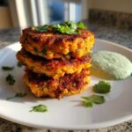 Three golden-brown Chickpea & Sweet Potato Fritters stacked high on a white plate with green dipping sauce.