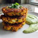 A stack of three golden-brown Chickpea & Sweet Potato Fritters served with a side of creamy green dipping sauce.