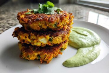 A stack of three golden-brown Chickpea & Sweet Potato Fritters served with a side of creamy green dipping sauce.