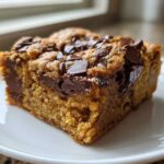 A thick, moist square of Chocolate Chip Banana Bars topped with melted chocolate chips, served on a white plate.