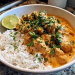 Close-up of a white bowl filled with creamy Coconut Chicken Bowl served over white rice, garnished with cilantro and a lime wedge.