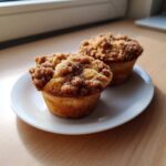 Two delicious Coffee Cake Muffins with a thick, sugary cinnamon crumb topping sitting on a white plate.