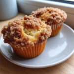 Two Coffee Cake Muffins with a thick, sugary cinnamon crumb topping resting on a small white plate.