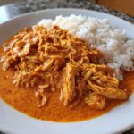 A close-up of shredded chicken in rich, orange Cajun butter sauce served next to white rice, showcasing the Creamy Crockpot Cajun Butter Chicken.