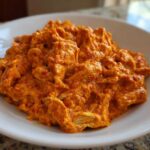 A close-up of shredded chicken coated in a thick, vibrant orange sauce, representing Creamy Crockpot Cajun Butter Chicken.