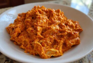 A close-up of shredded chicken coated in a thick, vibrant orange sauce, representing Creamy Crockpot Cajun Butter Chicken.