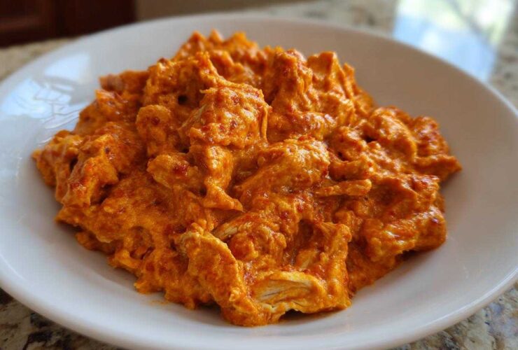 A close-up of shredded chicken coated in a thick, vibrant orange sauce, representing Creamy Crockpot Cajun Butter Chicken.