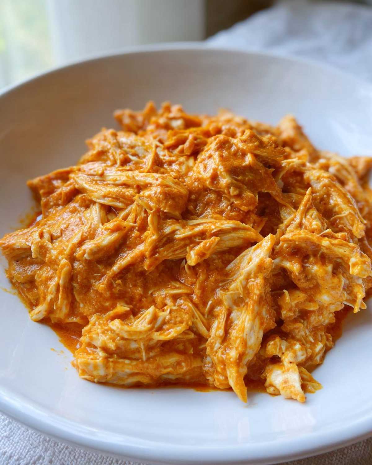 Close-up of shredded chicken coated in a rich, orange, creamy sauce, ready to serve, featuring Creamy Crockpot Cajun Butter Chicken.