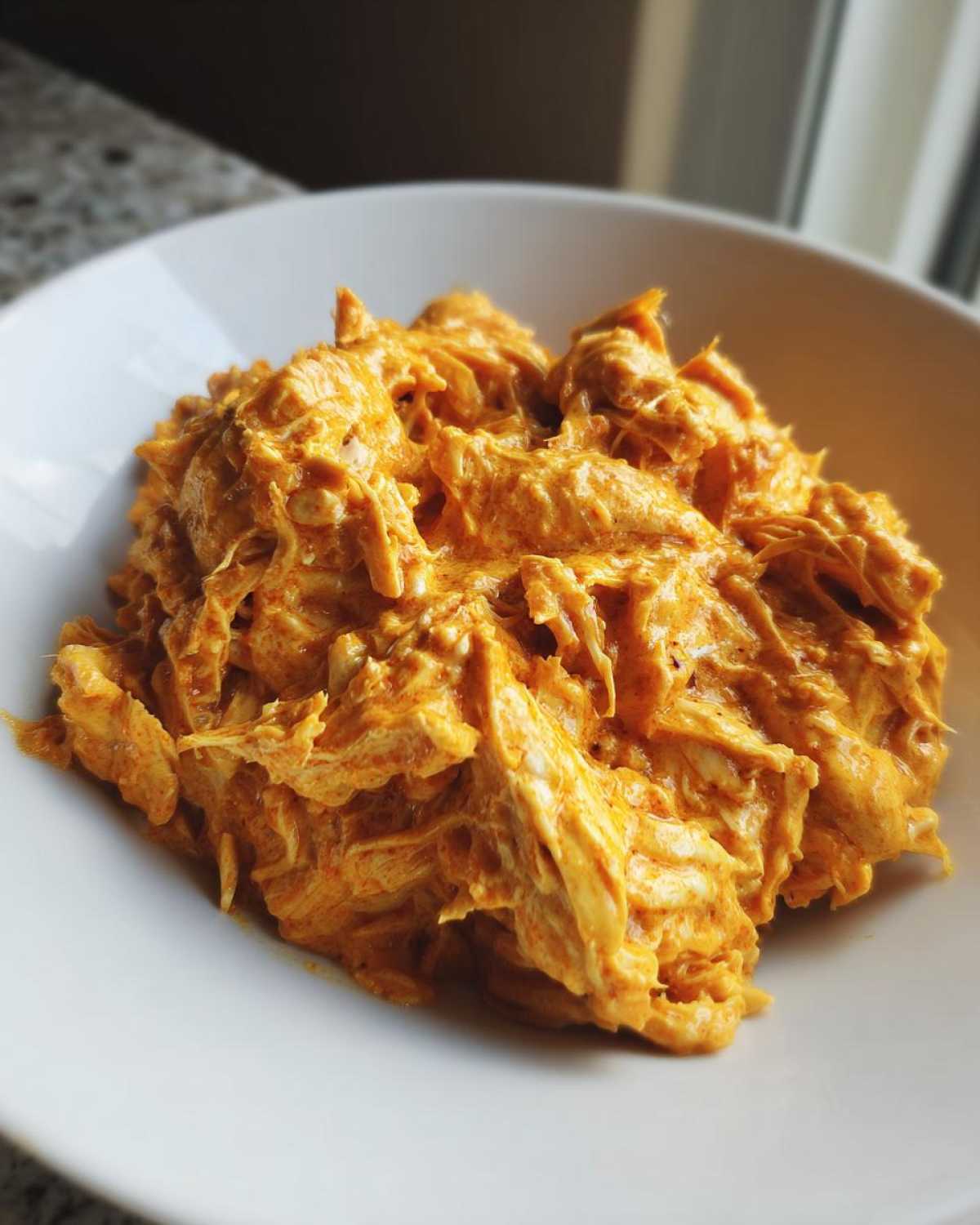 Close-up of shredded chicken coated in a rich, orange, creamy sauce, representing Creamy Crockpot Cajun Butter Chicken.