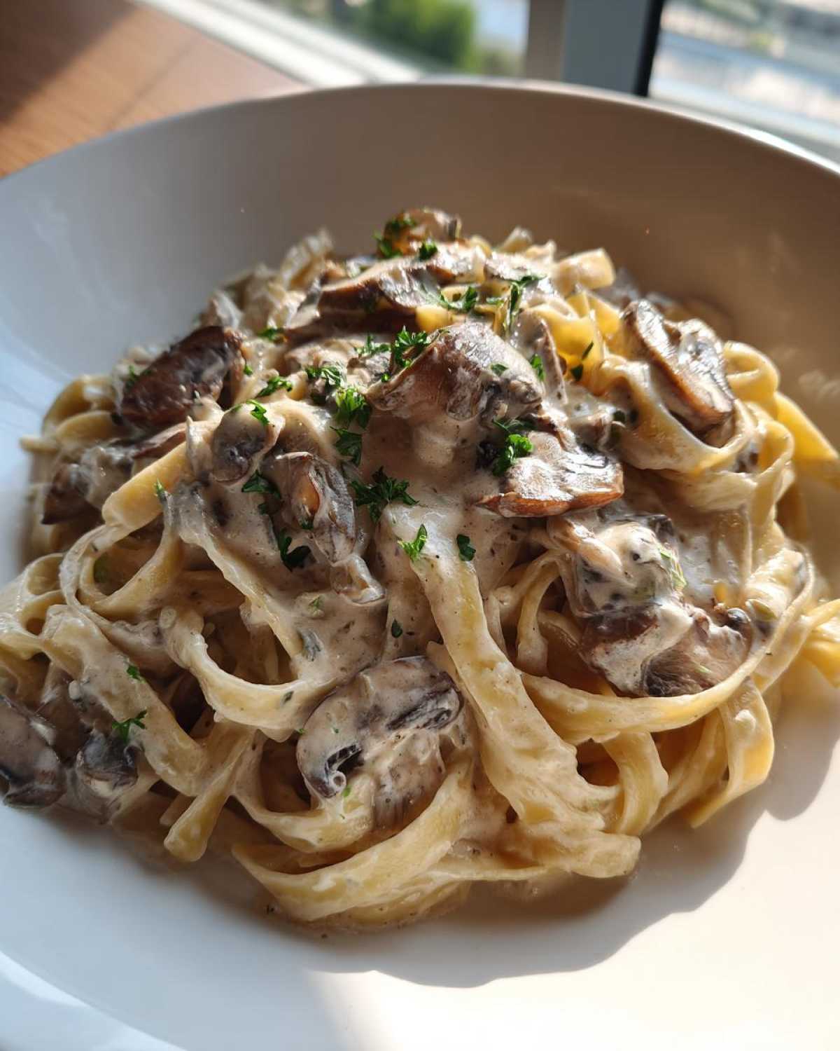 A close-up shot of fettuccine pasta coated in a rich, creamy garlic mushroom sauce, garnished with fresh parsley.