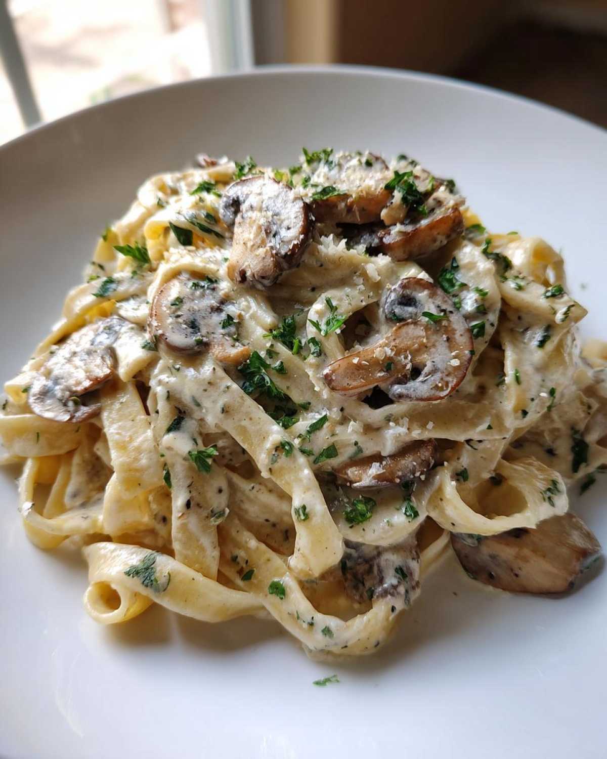 A serving of rich Creamy Garlic Mushroom Pasta featuring fettuccine noodles coated in a white sauce, topped with sliced mushrooms and fresh parsley.