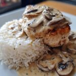 A close-up of a perfectly cooked piece of Creamy Smothered Chicken and Rice, topped with mushroom sauce.
