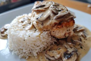 A close-up of a perfectly cooked piece of Creamy Smothered Chicken and Rice, topped with mushroom sauce.