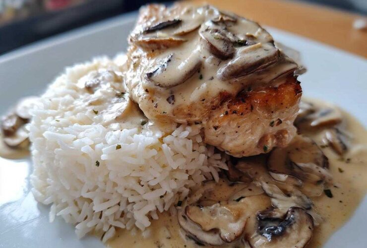 A close-up of a perfectly cooked piece of Creamy Smothered Chicken and Rice, topped with mushroom sauce.