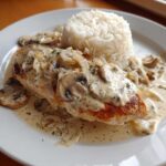 A perfectly cooked piece of Creamy Smothered Chicken and Rice topped with mushroom cream sauce on a white plate.