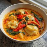 Close-up of Creamy Thai Red Curry Dumpling Soup featuring dumplings, red peppers, and spinach in a rich orange broth.