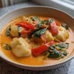 Close-up of Creamy Thai Red Curry Dumpling Soup featuring dumplings, spinach, and red peppers in a light-colored bowl.
