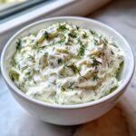 A close-up of thick, creamy Tzatziki Sauce in a white bowl, generously garnished with fresh dill.
