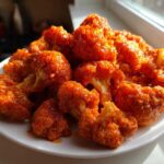 A mound of bright orange, saucy Crispy Air Fryer Buffalo Cauliflower Wings piled high on a white plate.