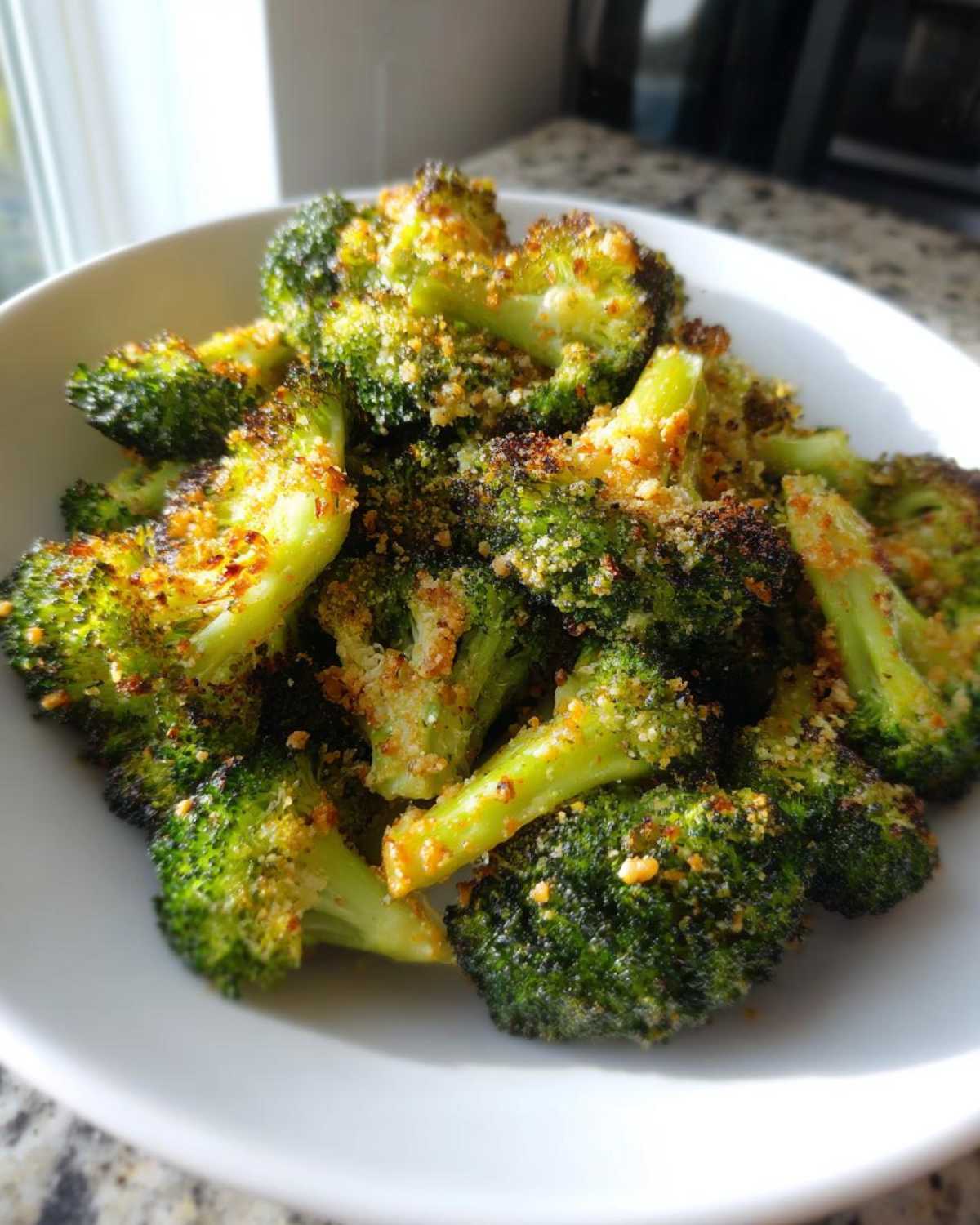 Close-up of roasted Garlic Parmesan Broccoli florets coated in crispy cheese topping served in a white bowl.