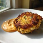 Close-up of a perfectly seared, crispy Maryland Crab Cakes served next to a dollop of orange Remoulade Sauce.