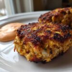 Close-up of a perfectly seared, crispy Maryland Crab Cakes served with a dollop of pinkish Remoulade Sauce.