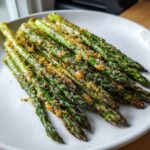 A close-up of bright green Crispy Roasted Asparagus A Side Dish for Christmas, topped with Parmesan cheese, served on a white plate.