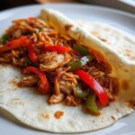 Close-up of shredded chicken and colorful bell peppers served in a soft tortilla for Crockpot Chicken Fajitas.