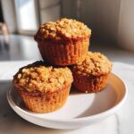 Three Delicious Healthy Banana Oatmeal Muffins stacked on a small white plate, topped with visible oats.