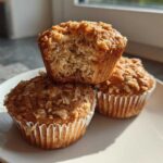 Three Delicious Healthy Banana Oatmeal Muffins stacked on a white plate, one muffin is broken open showing the texture.