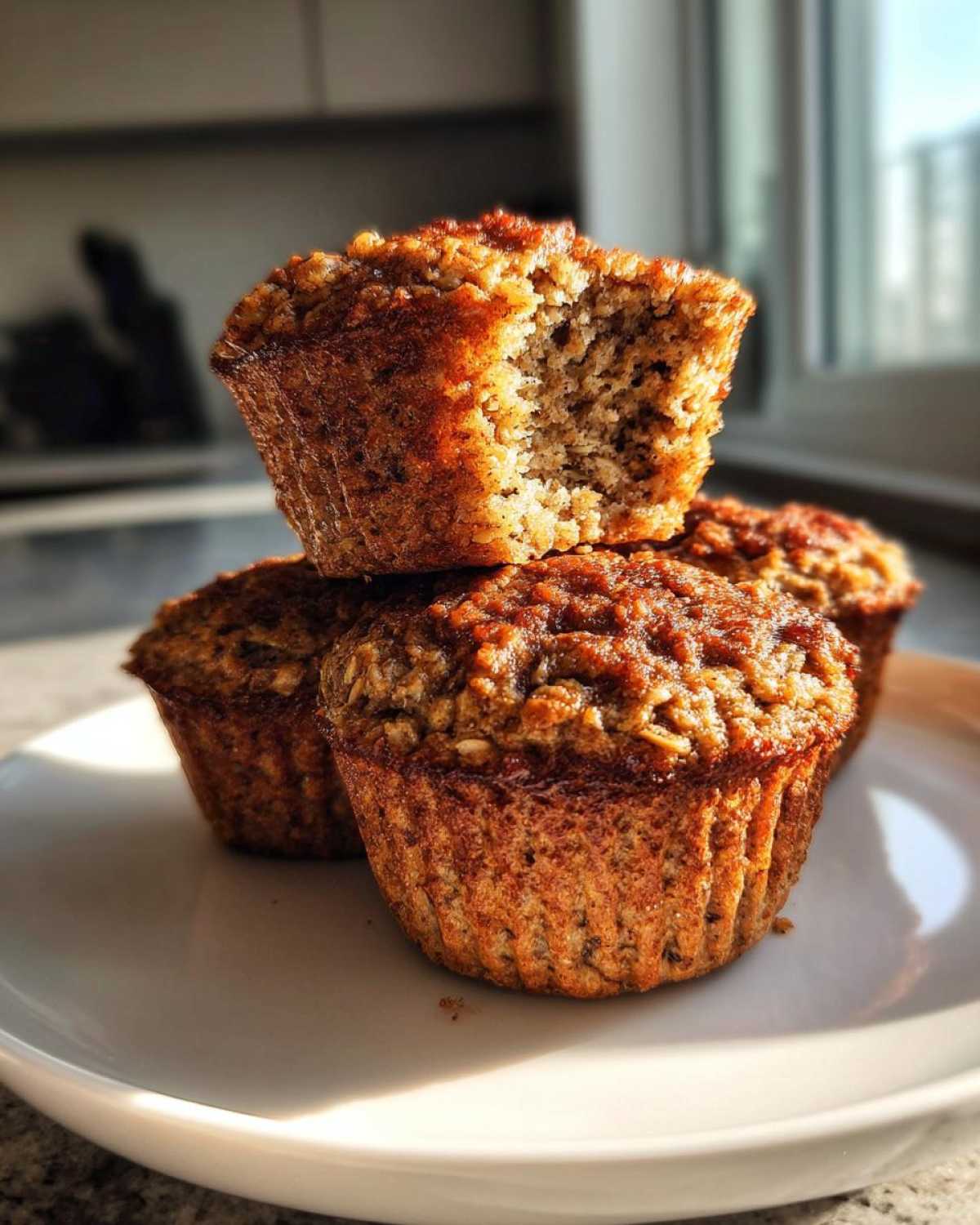 A stack of three Delicious Healthy Banana Oatmeal Muffins, one on top with a bite taken out, showing the texture.