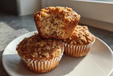 Three Delicious Healthy Banana Oatmeal Muffins stacked on a white plate, one muffin is broken open showing the texture.