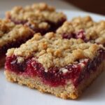 Close-up of three delicious Raspberry Crumb Bars showing the thick, bright red raspberry filling and crumbly oat topping.