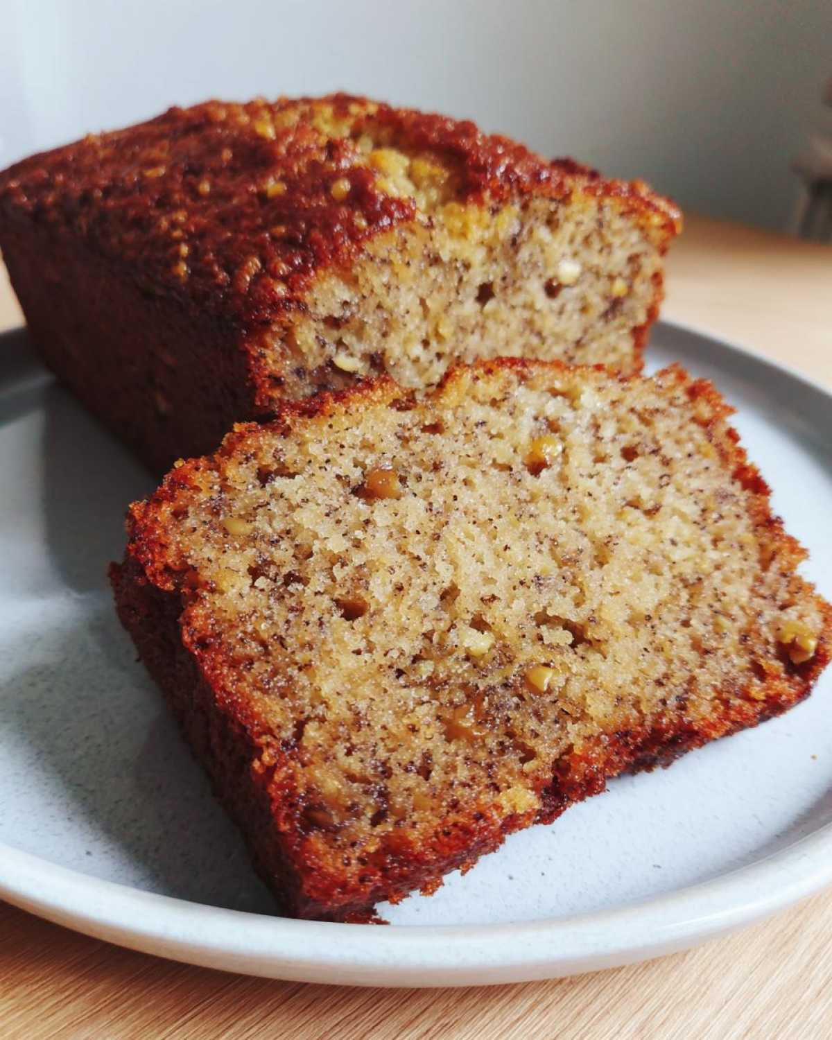 Close-up of a thick slice of moist Favorite Banana Bread on a plate, showing the speckled interior and caramelized crust.