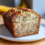 A close-up of a moist slice of Favorite Banana Bread showing the crumb texture and walnuts on top.