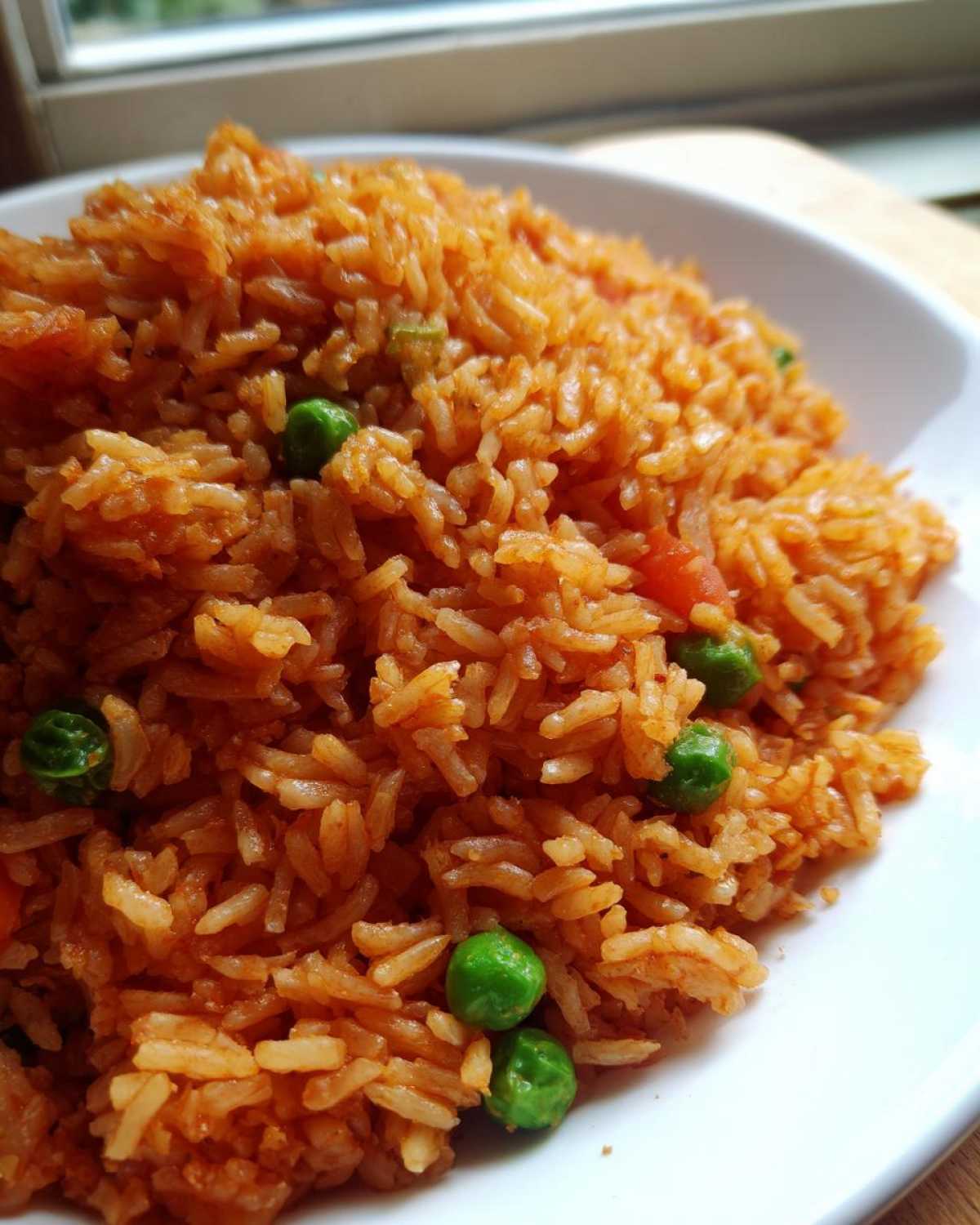 Close-up of fluffy Authentic Mexican Rice, showing orange-tinted grains mixed with bright green peas.