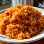 A close-up, featured image of a mound of fluffy Authentic Mexican Rice, bright orange-red, served on a white plate.