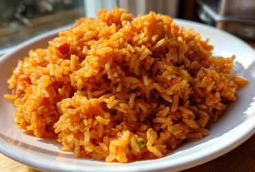 A close-up, featured image of a mound of fluffy Authentic Mexican Rice, bright orange-red, served on a white plate.