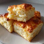 Close-up of three fluffy Buttermilk Biscuits stacked on a light gray plate, showing golden-brown tops and flaky interior.