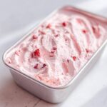 Close-up of light pink, fluffy Strawberry Mousse studded with small strawberry pieces, set in a rectangular metal container.
