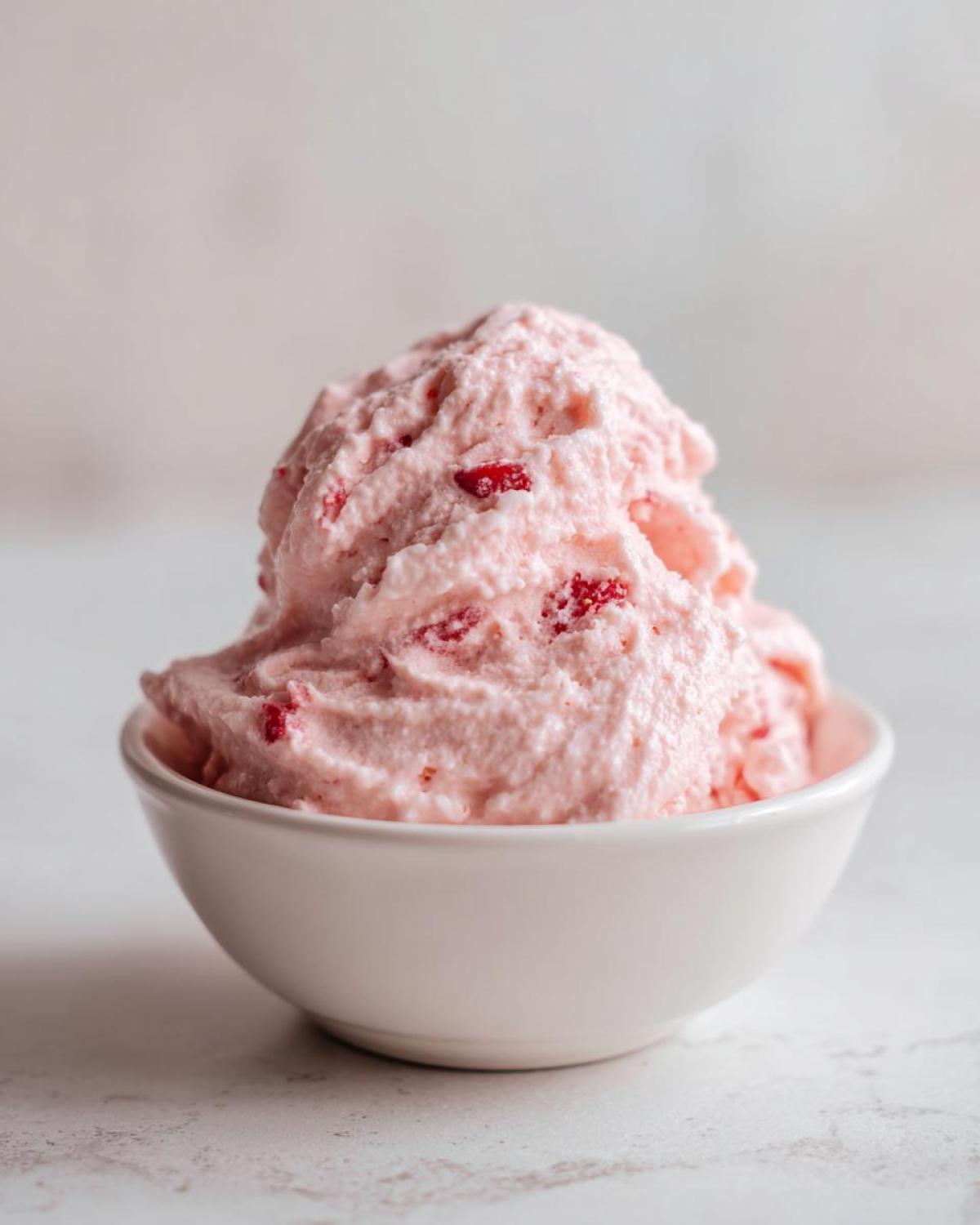 A generous scoop of light pink, fluffy Strawberry Mousse speckled with real strawberry pieces, served in a small white bowl.