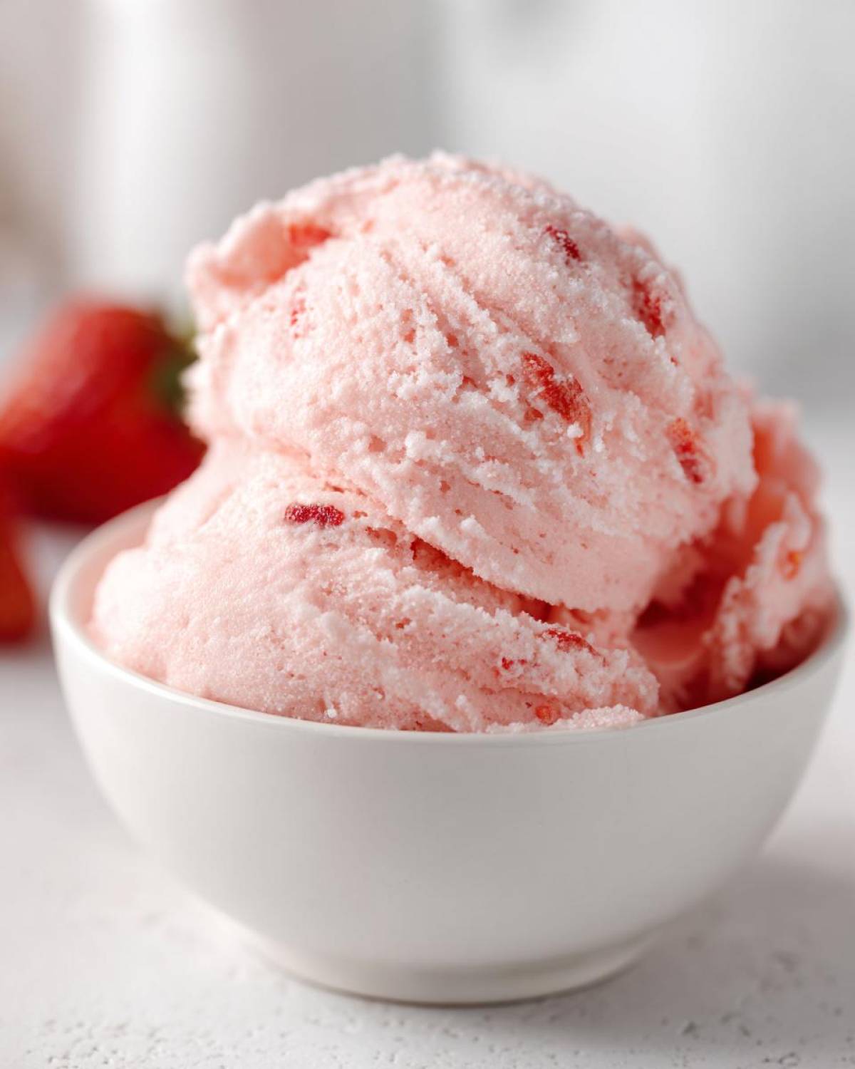 Close-up of fluffy pink Strawberry Mousse scooped into a small white bowl, with visible strawberry pieces.