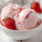 Two scoops of light pink, fluffy Strawberry Mousse garnished with a fresh strawberry in a white bowl.