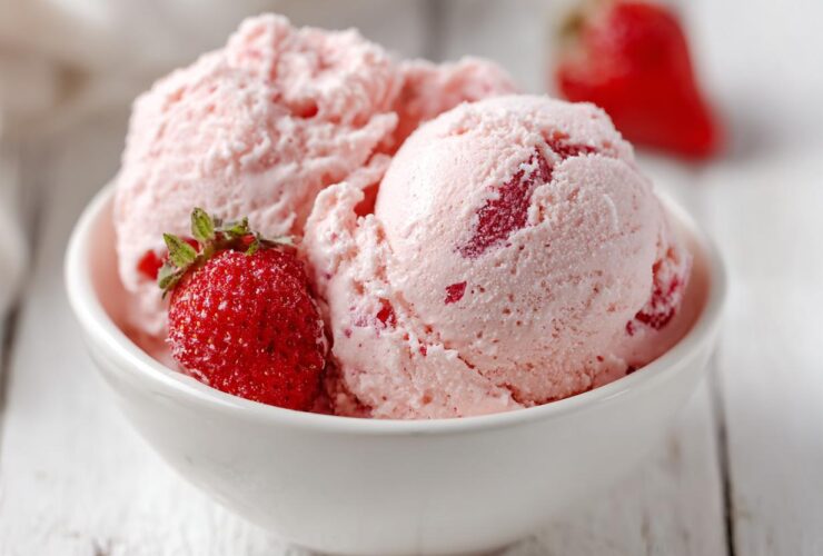 Two scoops of light pink, fluffy Strawberry Mousse garnished with a fresh strawberry in a white bowl.