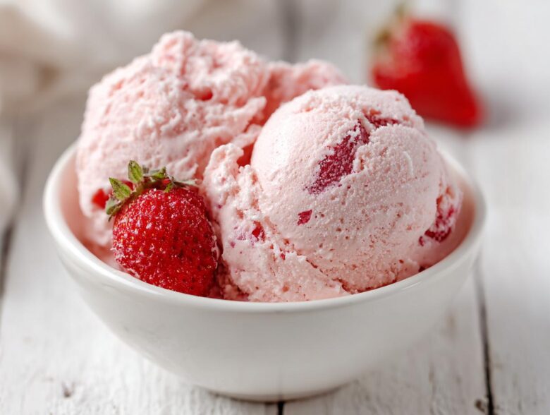 Two scoops of light pink, fluffy Strawberry Mousse garnished with a fresh strawberry in a white bowl.