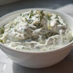 A close-up of thick, creamy Tzatziki Sauce garnished with fresh dill, served in a white bowl.
